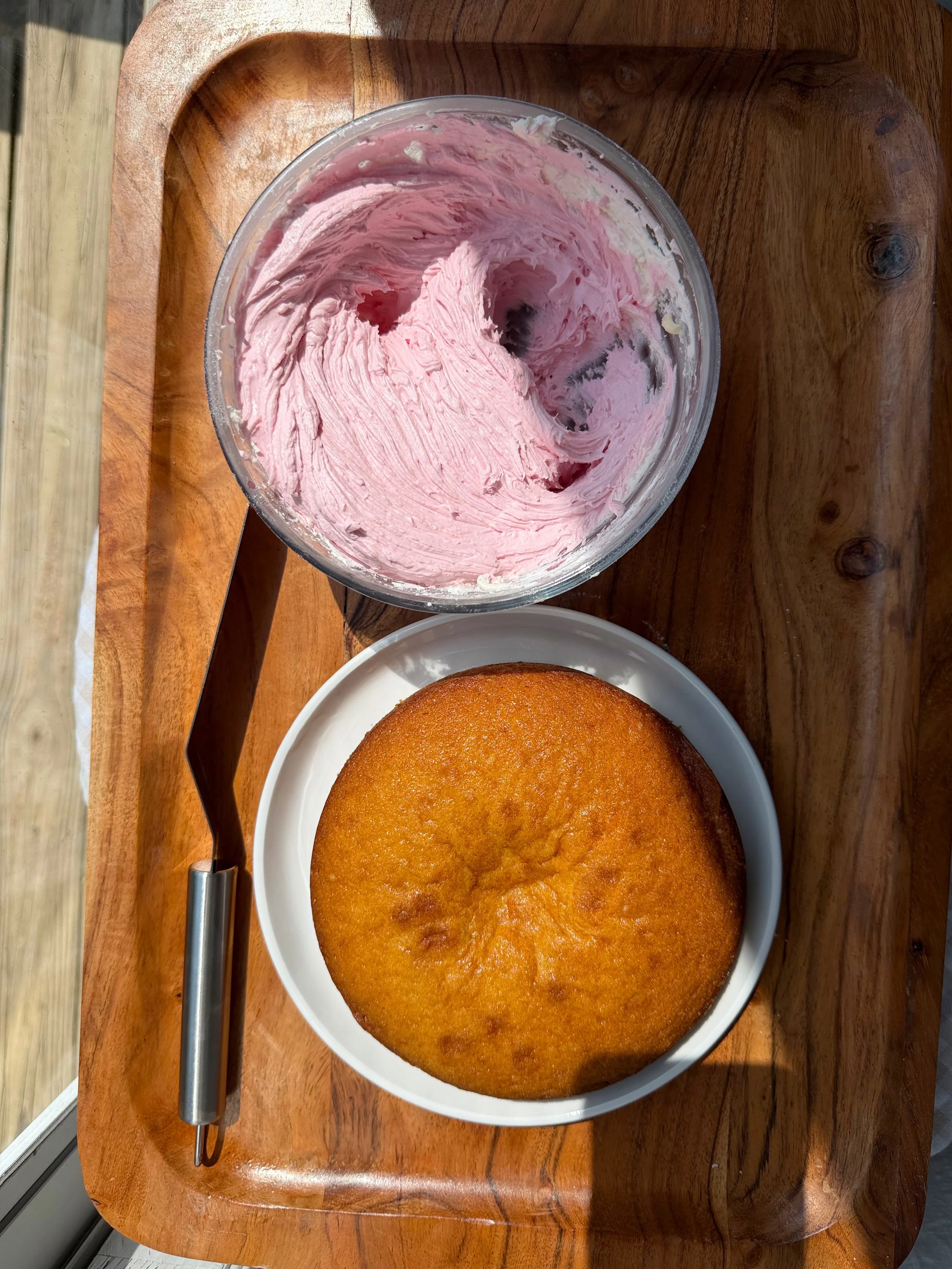 Raspberry buttercream and baked cake on wood cutting board. 