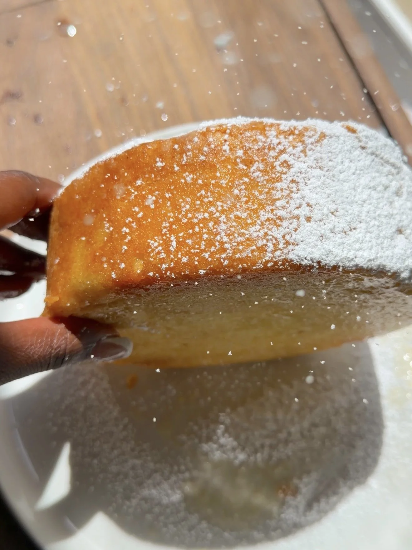 Hand holding cake on its side and rolling it in powdered sugar. 