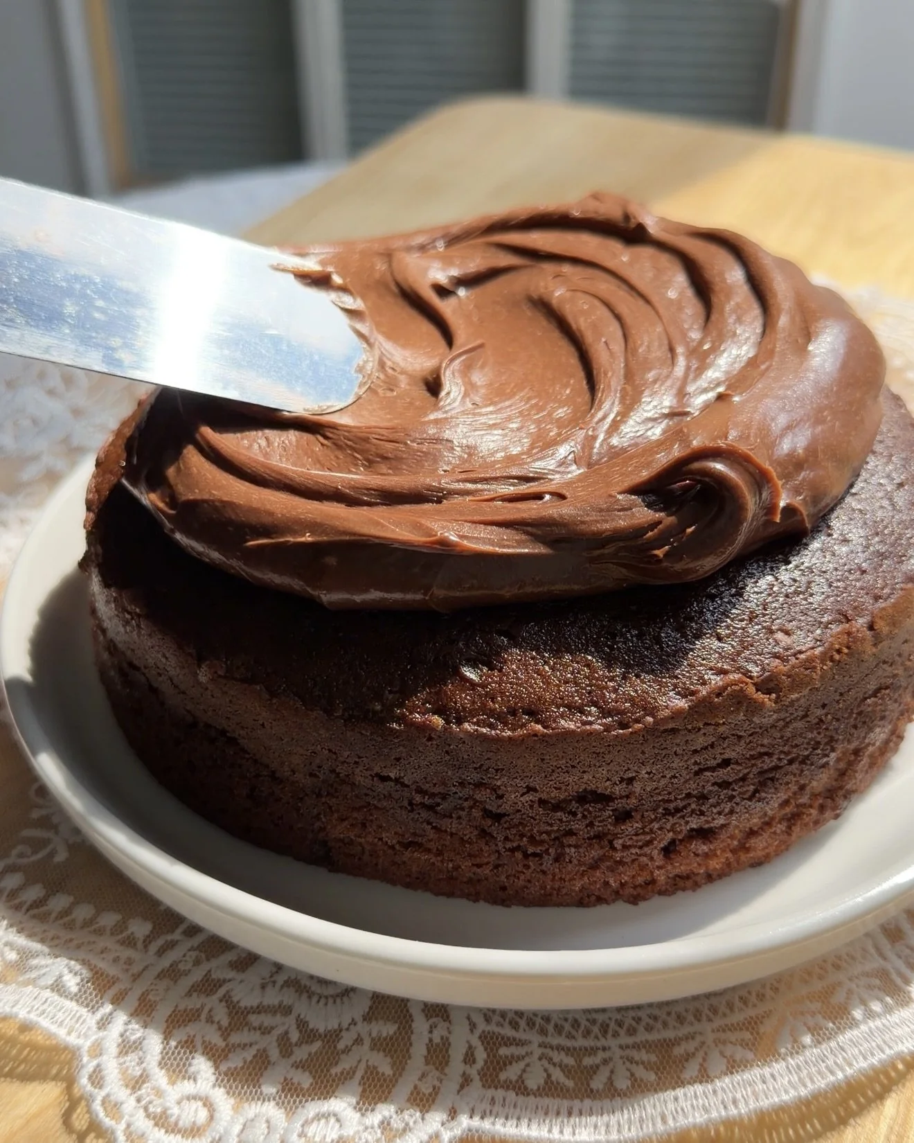 Chocolate buttercream being spread over a cooled single layer cake