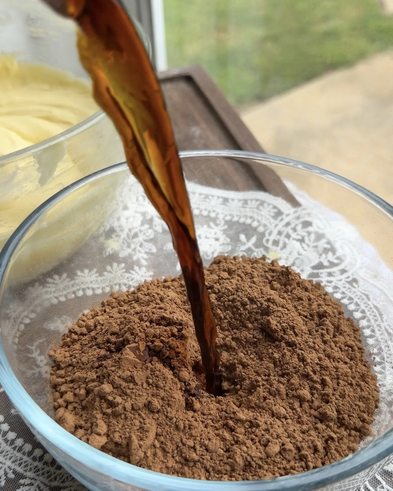 Cocoa powder being bloomed with hot coffee in small glass mixing bowl.