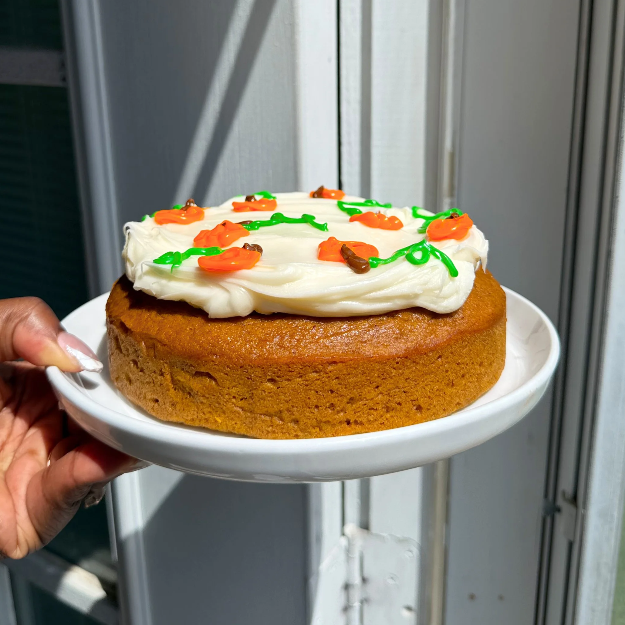 Hand holding white plate with Single layer pumpkin cake sliced and topped with cream cheese frosting