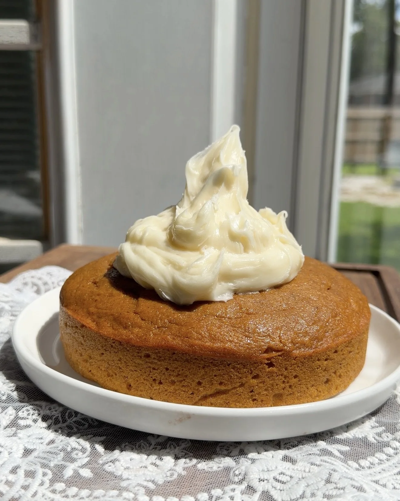 Cream cheese frosting is being spread evenly over the top of a cooled single layer pumpkin cake.