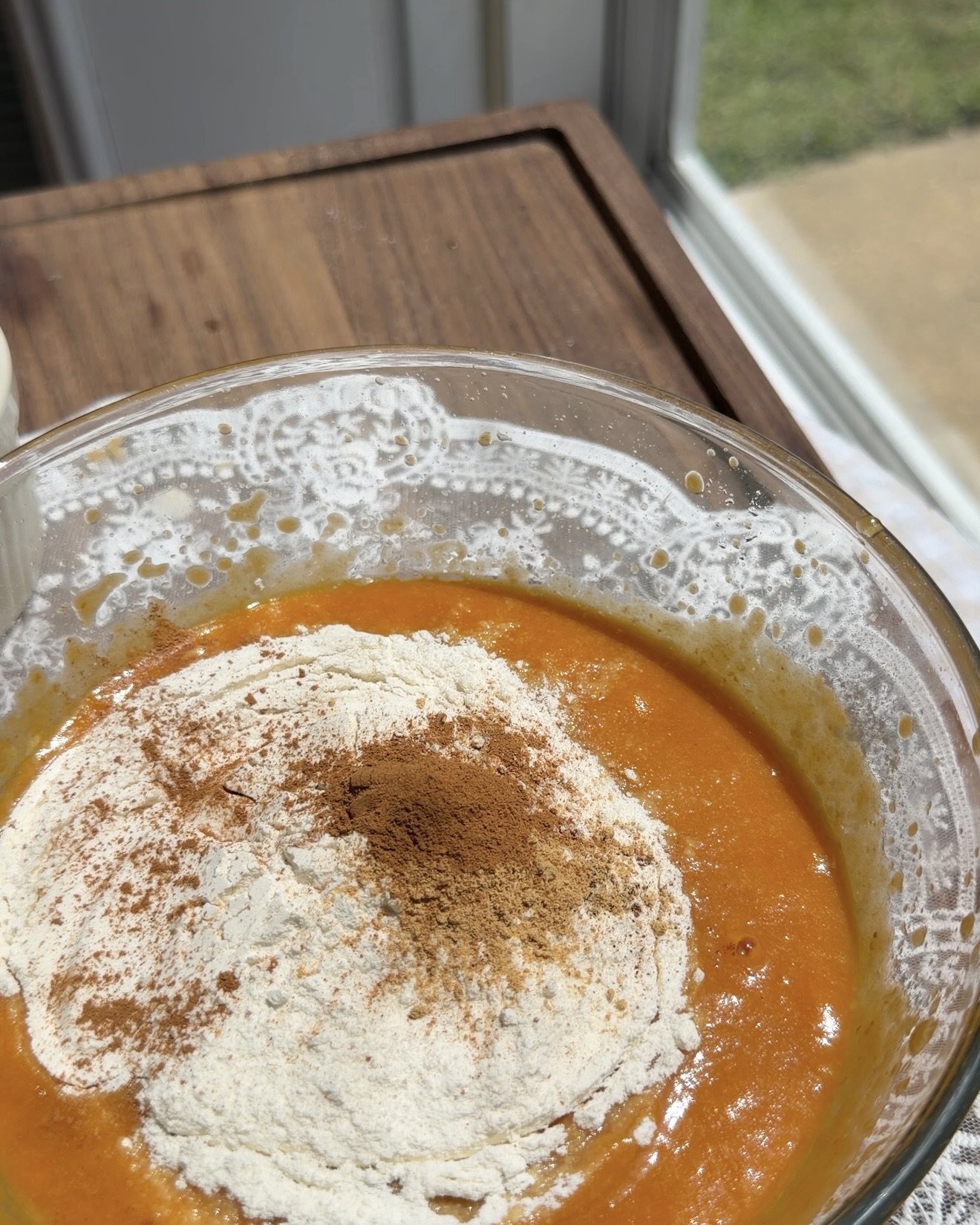 The dry ingredients are being added to the pumpkin mixture in a clear glass bowl and gently mixed until just combined.