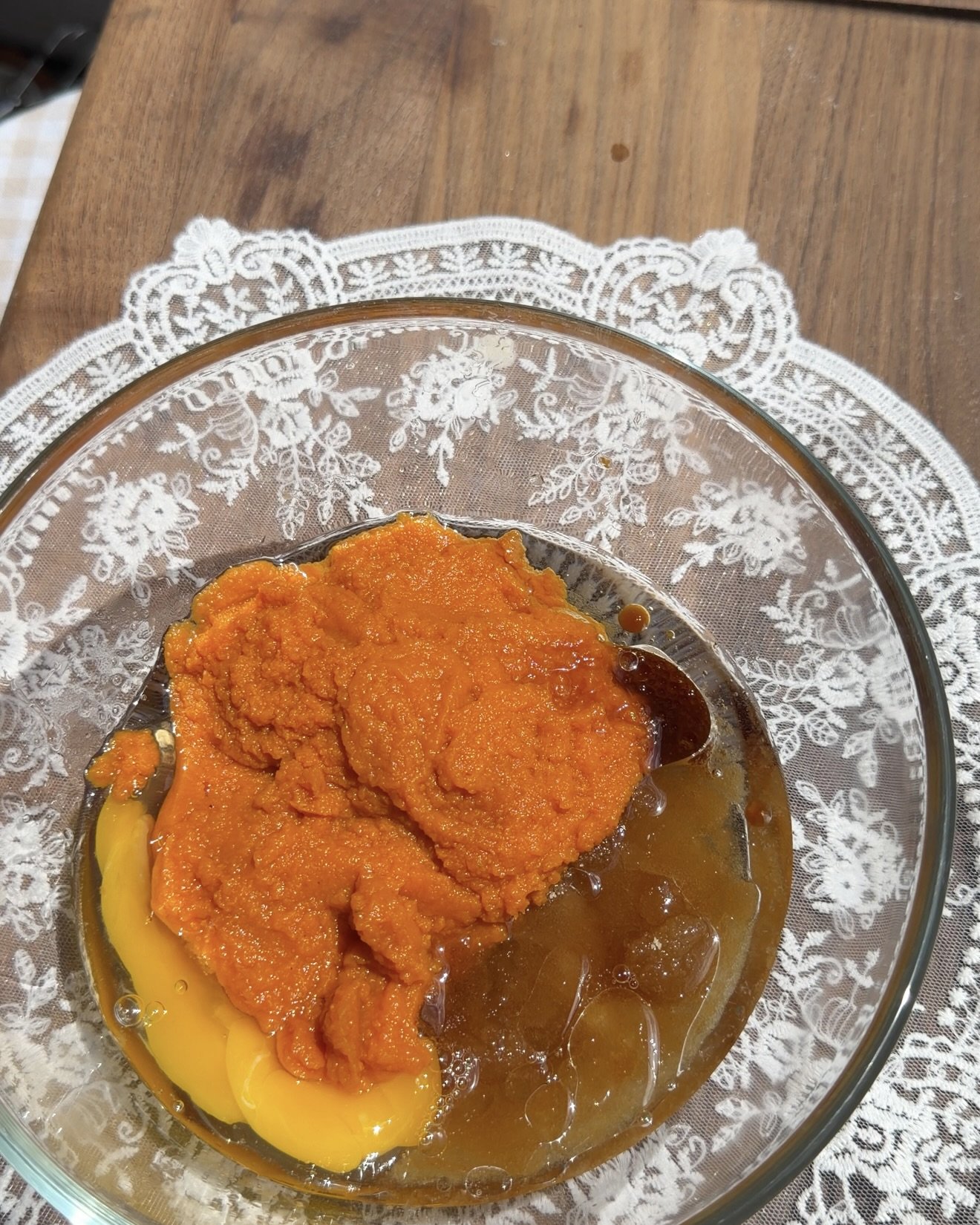 Pumpkin puree, granulated sugar, brown sugar, oil, and vanilla are being mixed together in a clear glass bowl until smooth.