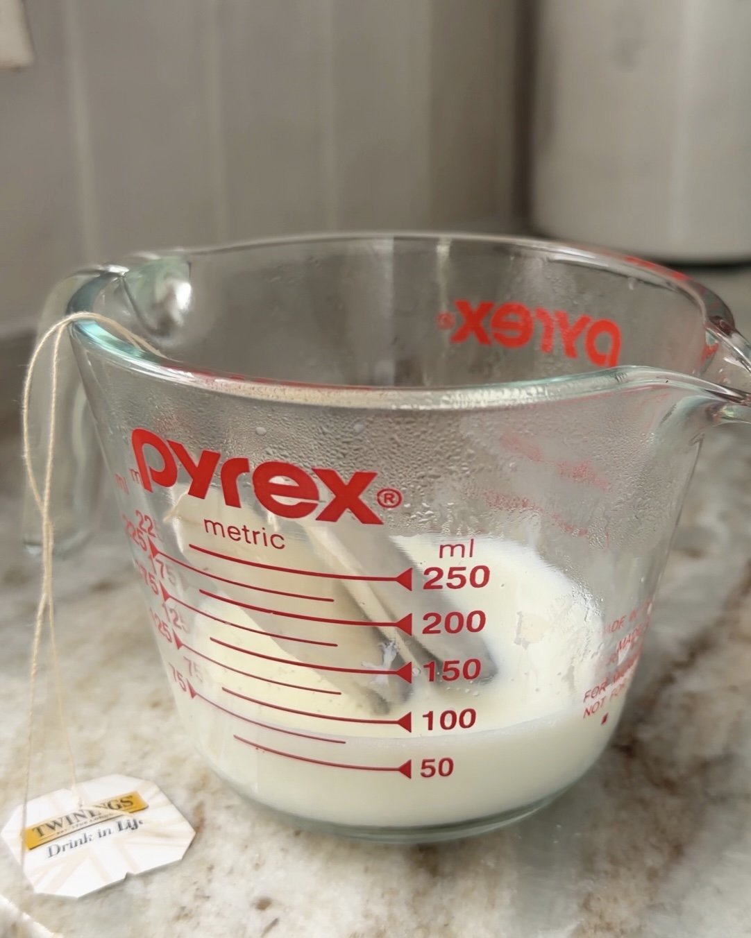 Glass pyrex measuring glass with 1/4 cup of milk and two steeping chai tea bags. 
