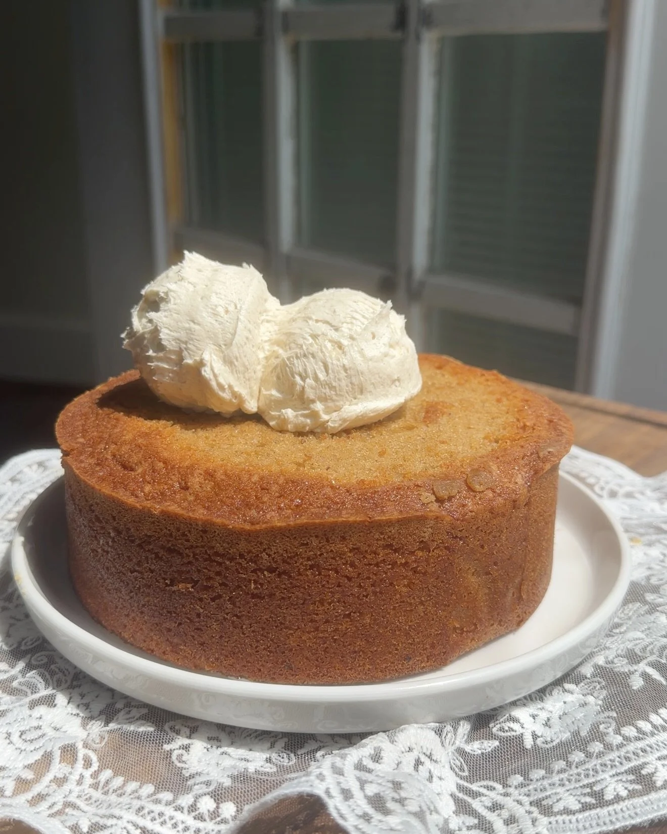 White plate with baked chai cake and two scoops of frosting on top. 