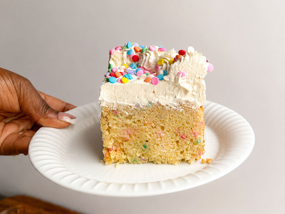 Hand holding white fluted plate with a slice of funfetti cake