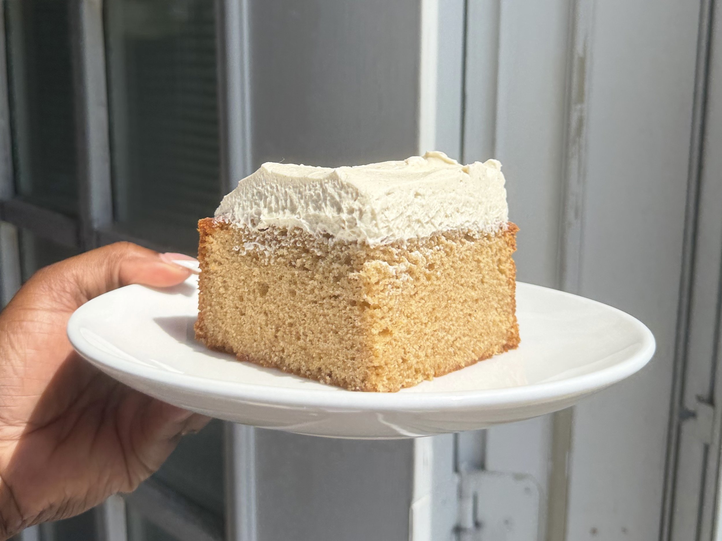 Hand holding white plate with Mini single layer chai latte cake topped with chai buttercream