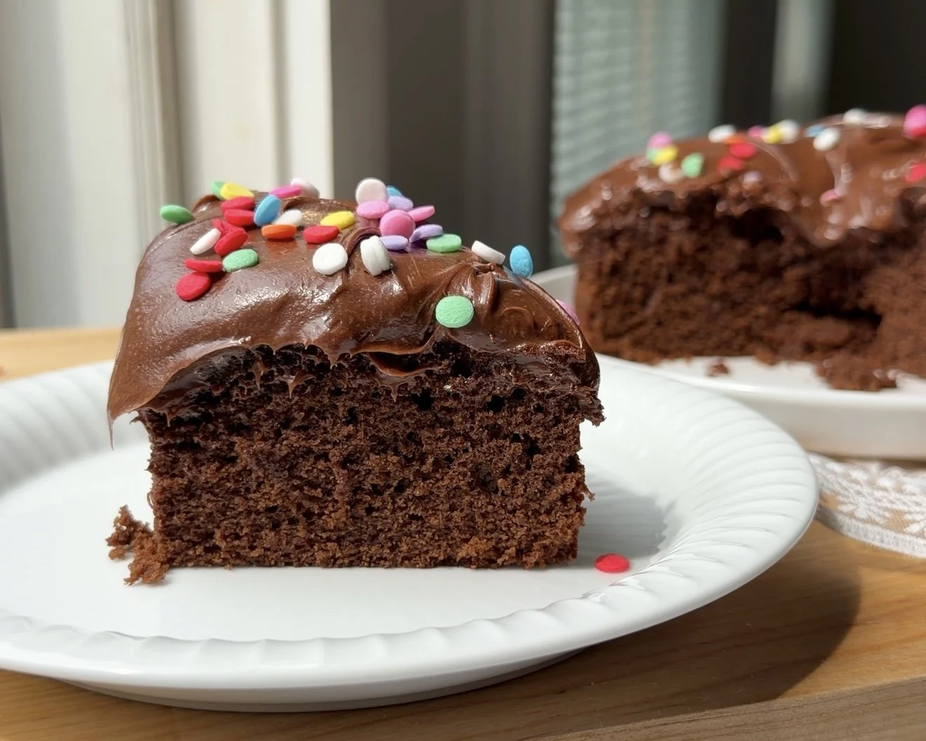 One slice of chocolate cake with frosting and sprinkles on white plate.