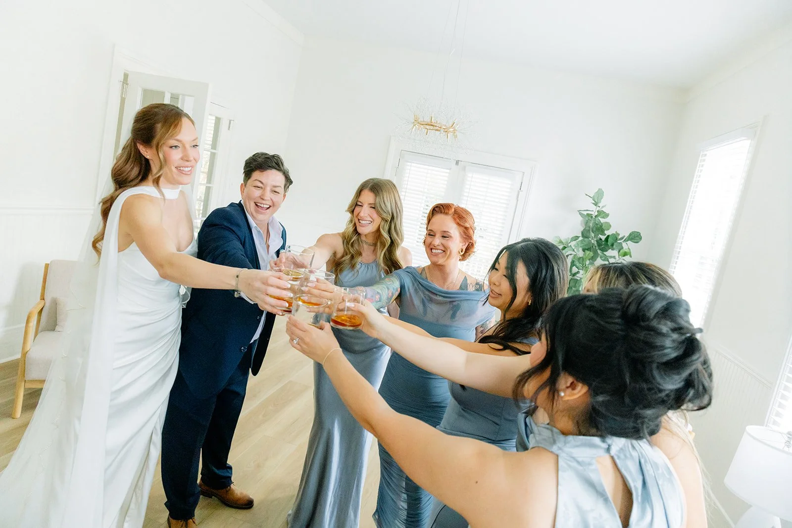 Group of women and one man raising glasses in a toast during a celebratory gathering in a bright room.