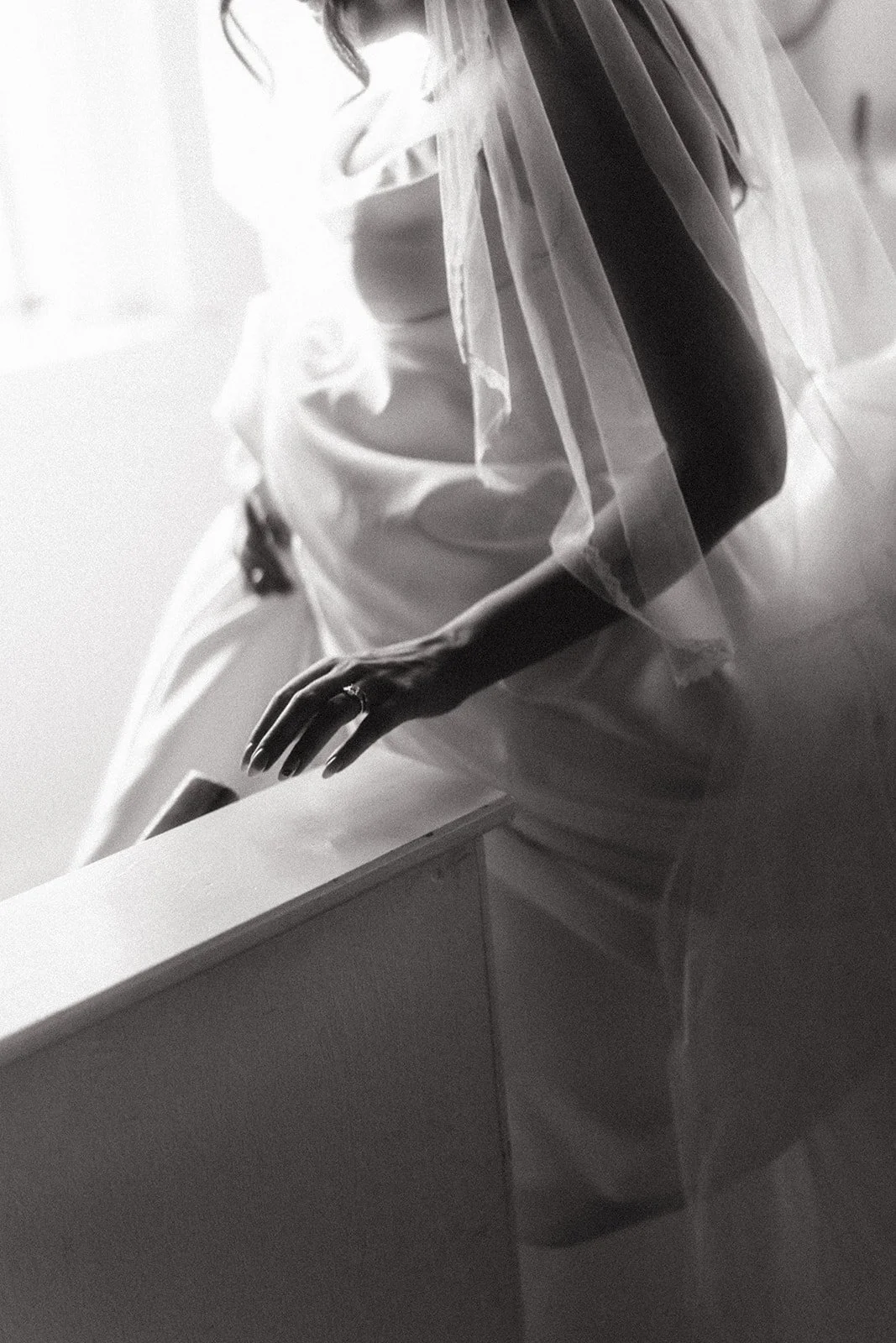 Black and white photo of a pregnant woman wearing a wedding ring, sitting on a hospital bed with a hospital bracelet on her wrist.