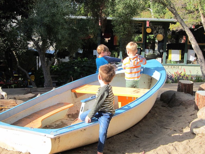Children playing on a sandbox boat in a park.