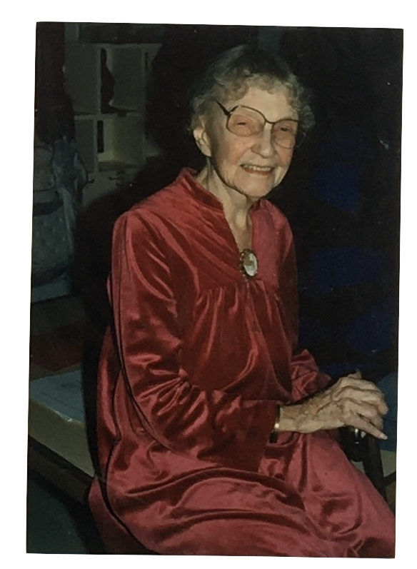 An elderly woman with glasses and curly hair, wearing a shiny red dress, sitting and smiling.