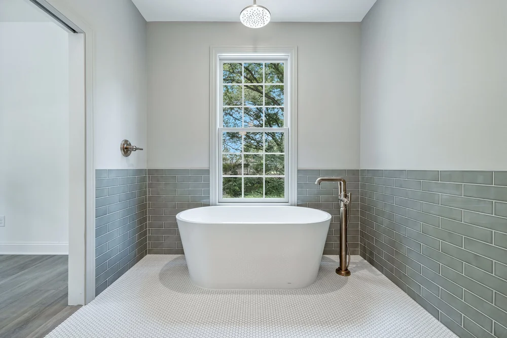 Bathroom with a freestanding tub, tiled walls, and a tall window
