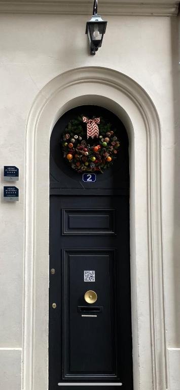 Black front door decorated with a Christmas wreath and a red and white bow, with a house number 2 and a QR code below, located under an arched entryway with exterior wall lights.