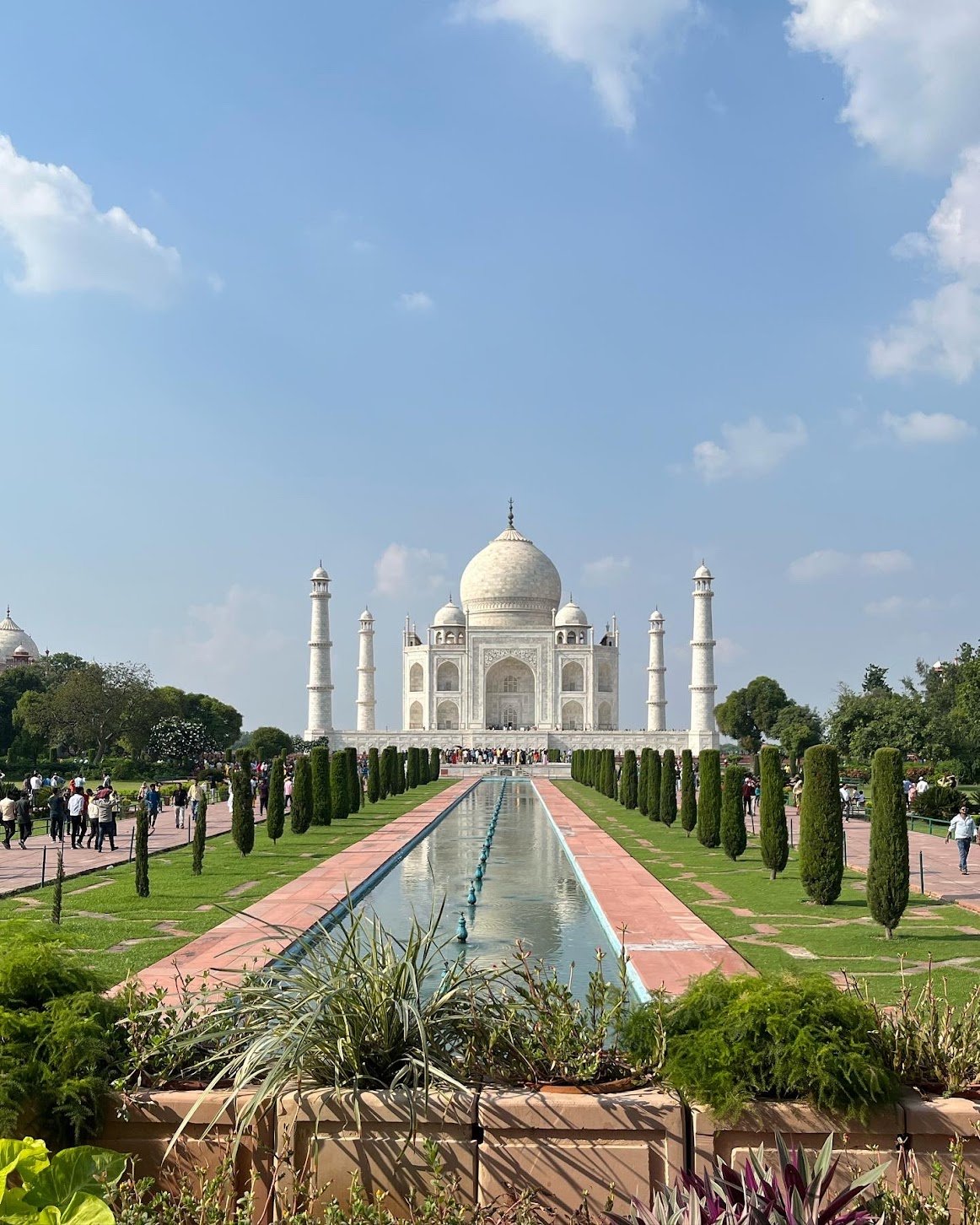 Taj Mahal in Agra, India, with reflecting pool and gardens in foreground, under a blue sky.