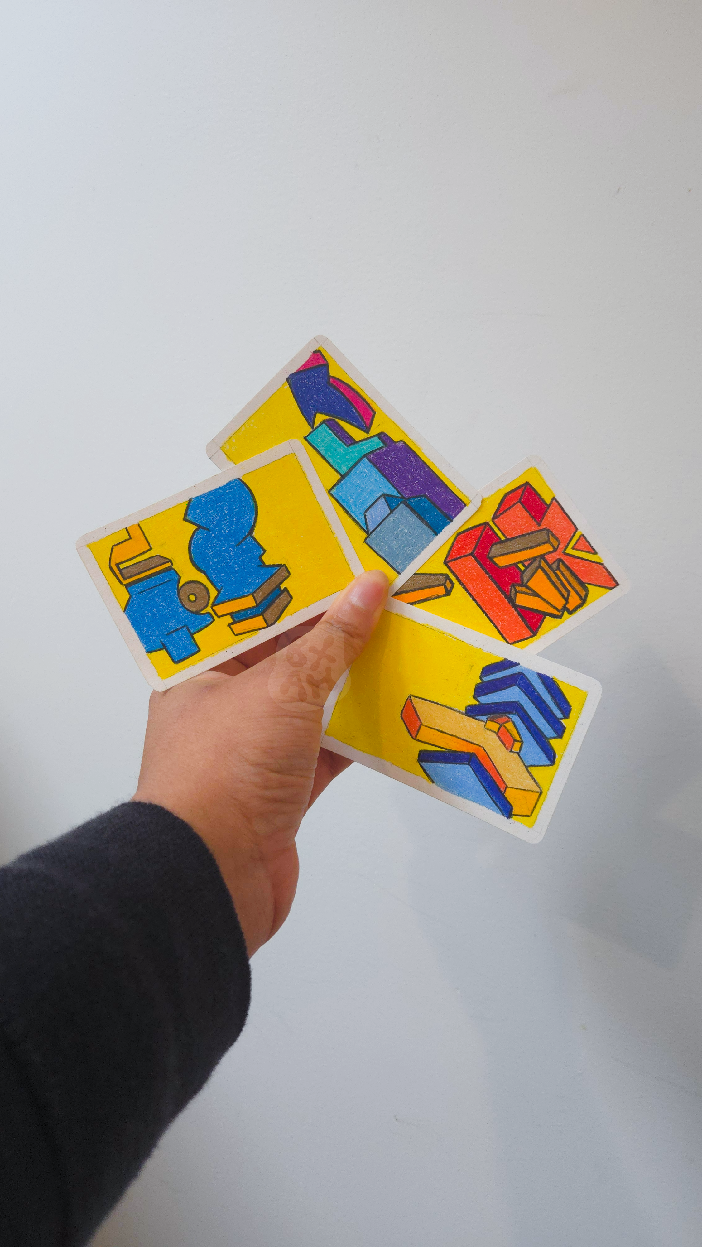 Hand holding four colorful cards with abstract block and arrow designs against a plain white background.