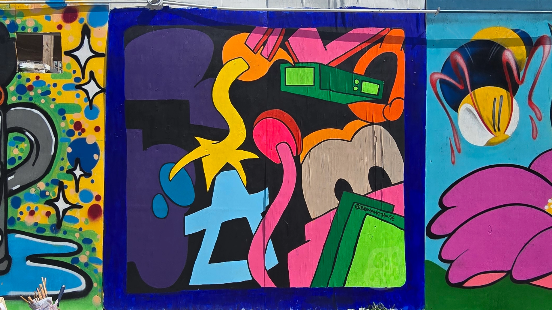 Colorful mural featuring abstract and cartoon elements, including a pink snake, a yellow star, a blue gear, a green rectangular object, and various vibrant shapes and patterns.