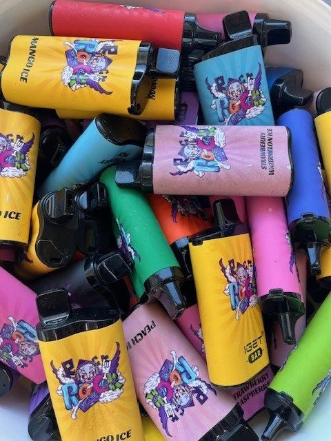 Colorful disposable vape pens with various flavors like mango, strawberry, peach, and raspberry, piled together.