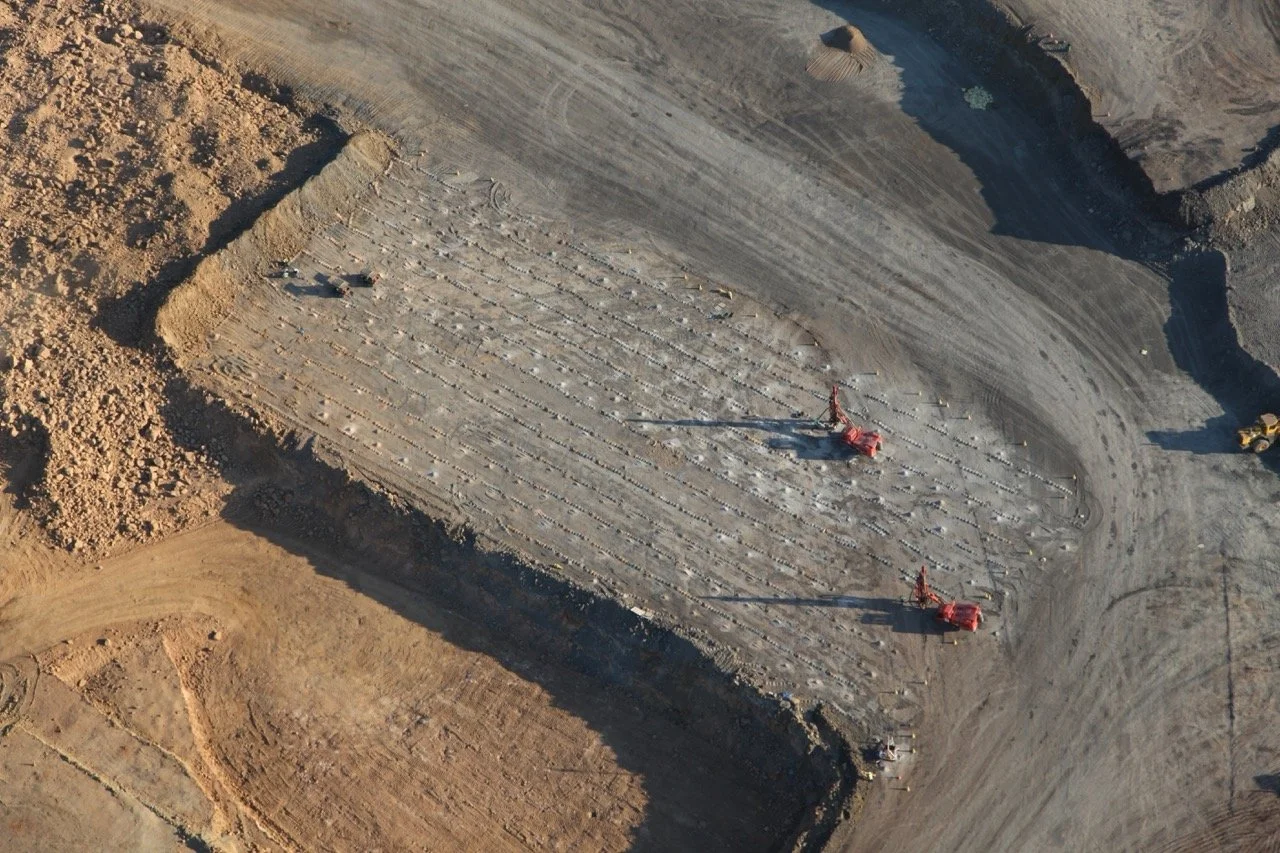 An aerial view of a construction site with two large red machines working on a flat, excavated area surrounded by dirt and soil.
