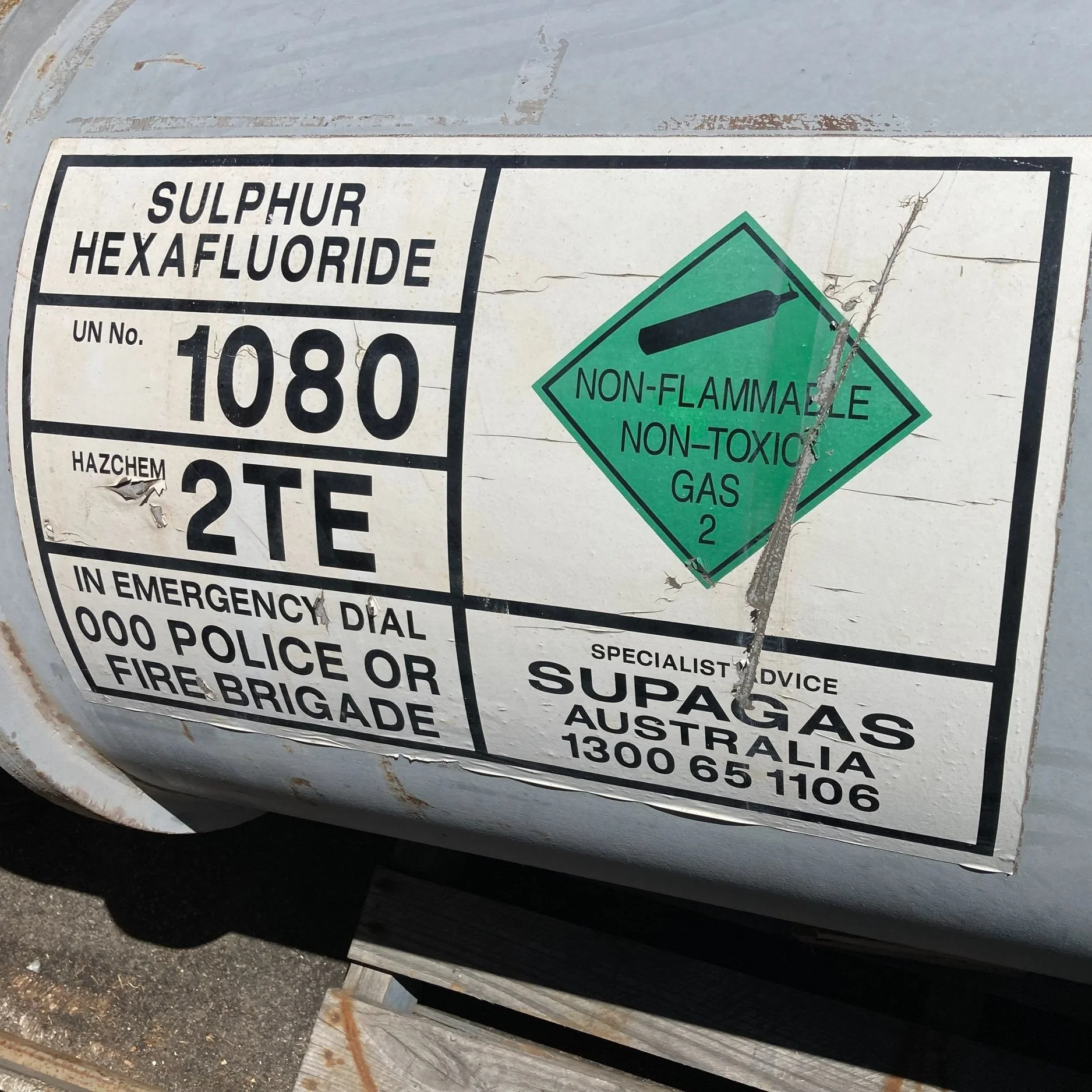 A gas cylinder label for sulfur hexafluoride, marked with UN number 1080 and hazard code 2TE. It indicates the gas is non-flammable and non-toxic. Emergency contact information for Supagas Australia is provided, including a phone number and emergency services contact instructions.