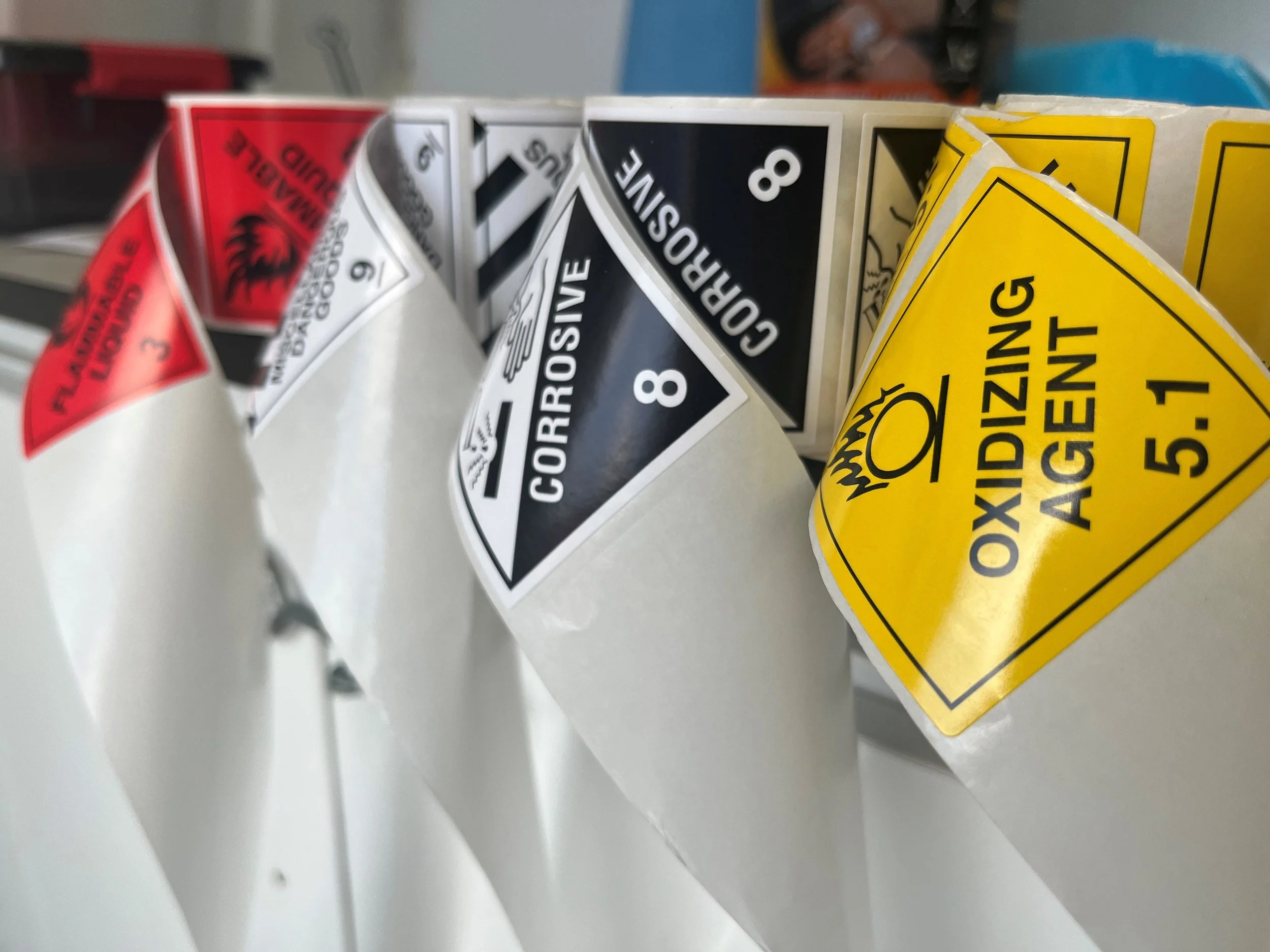 Close-up of various hazard labels, including "Flammable Liquid," "Corrosive," and "Oxidizing Agent."
