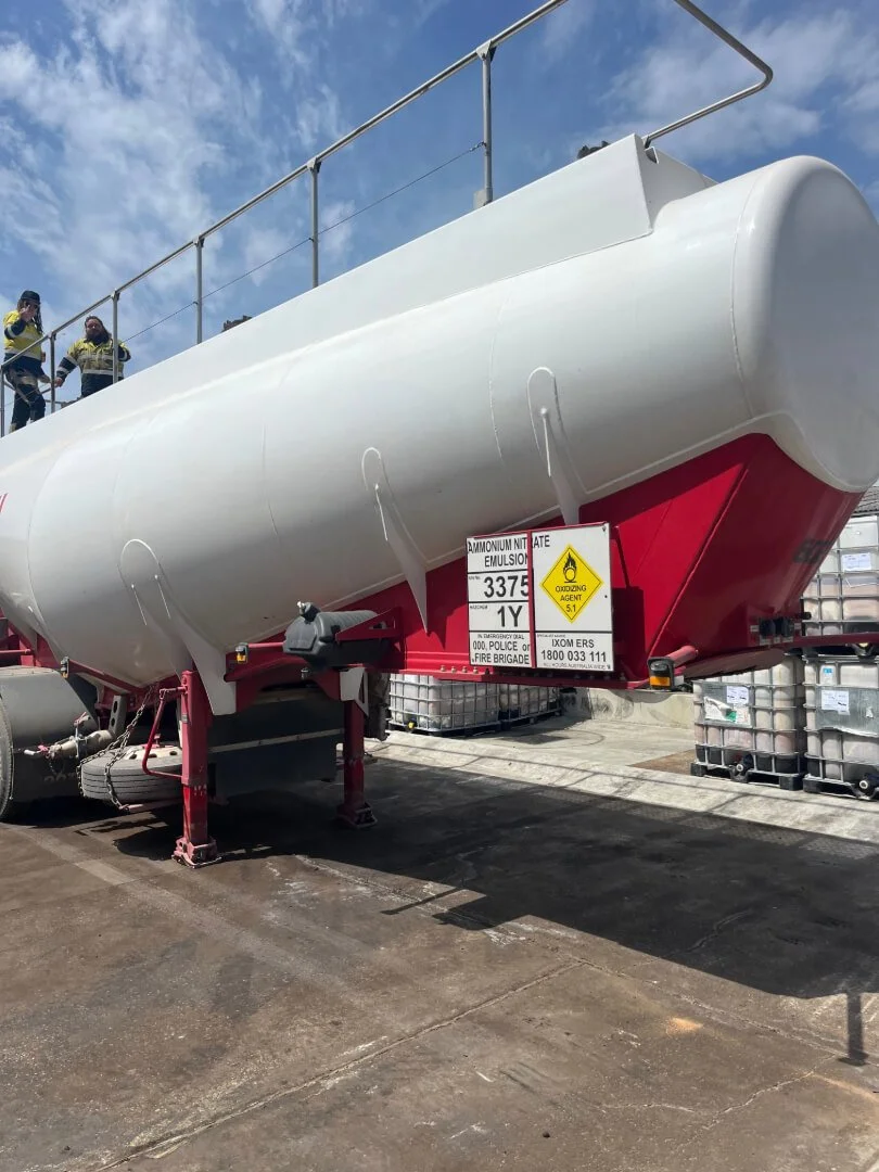 Flatbed truck carrying multiple large IBC containers under a cloudy sky.