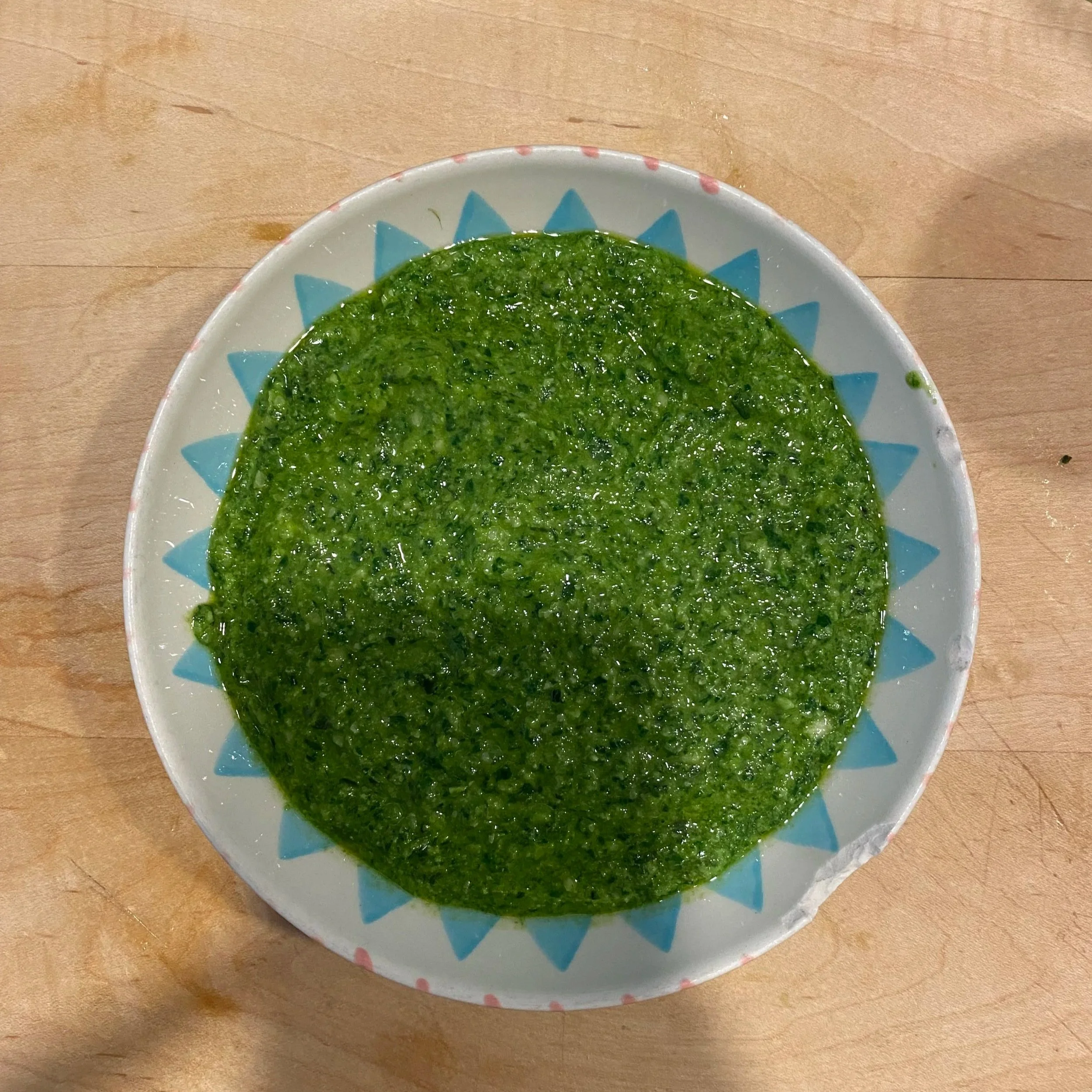 Bowl of green pesto sauce on a wooden table.