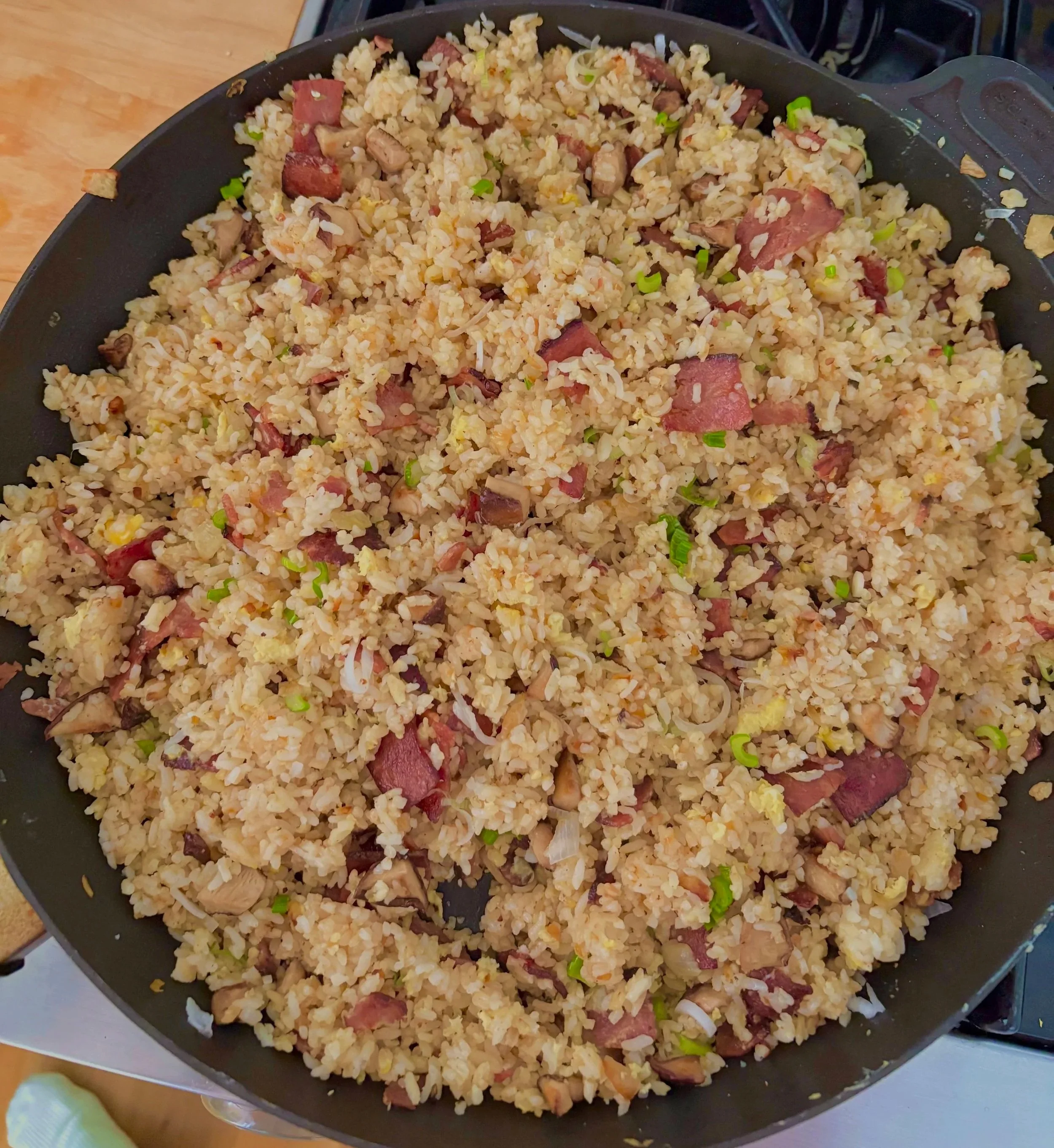 Cooked fried rice with pieces of turkey bacon, chopped green onions, and scrambled eggs in a black skillet.