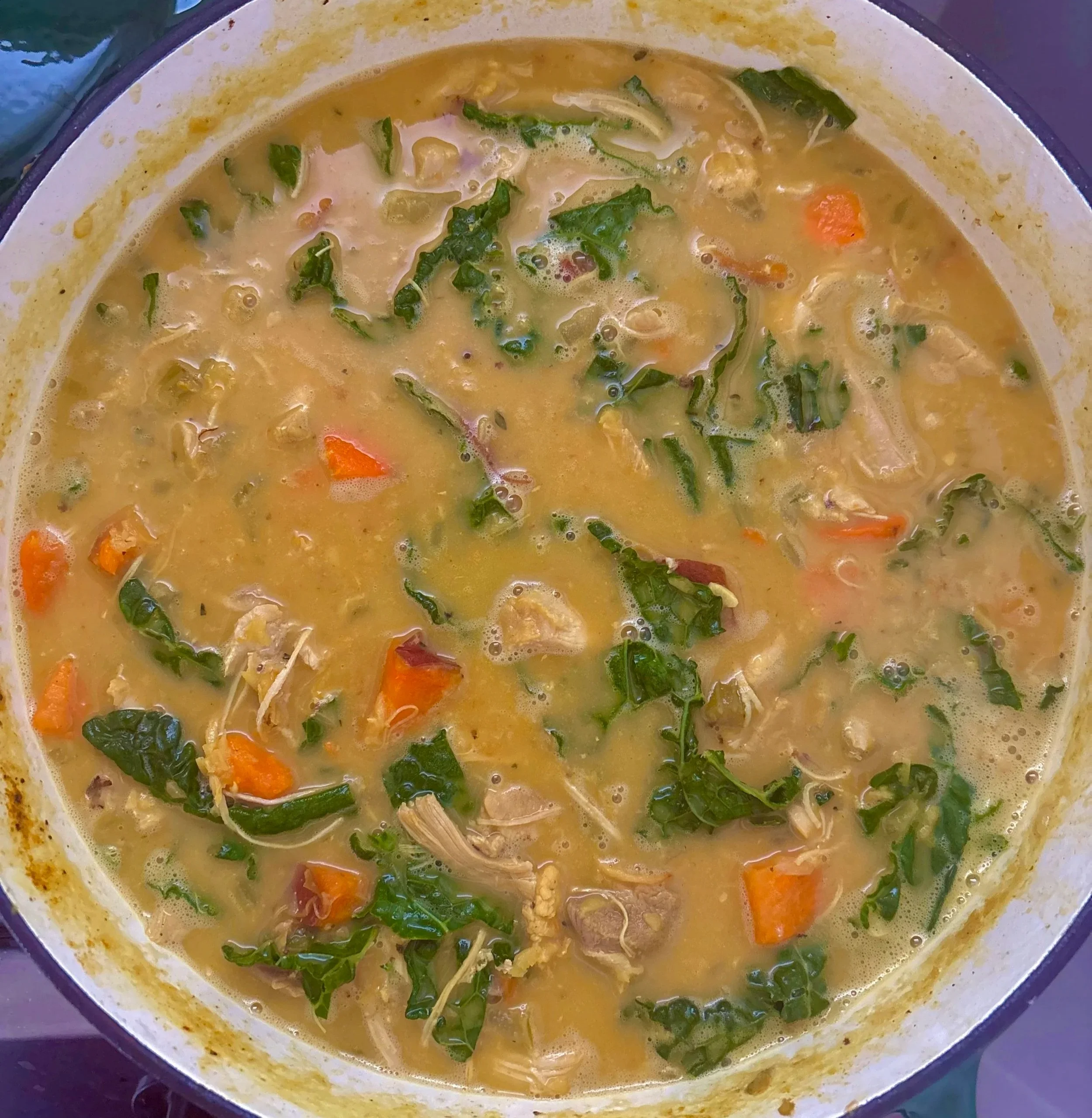 A pot of homemade chicken soup with chopped carrots, greens, and shredded chicken.