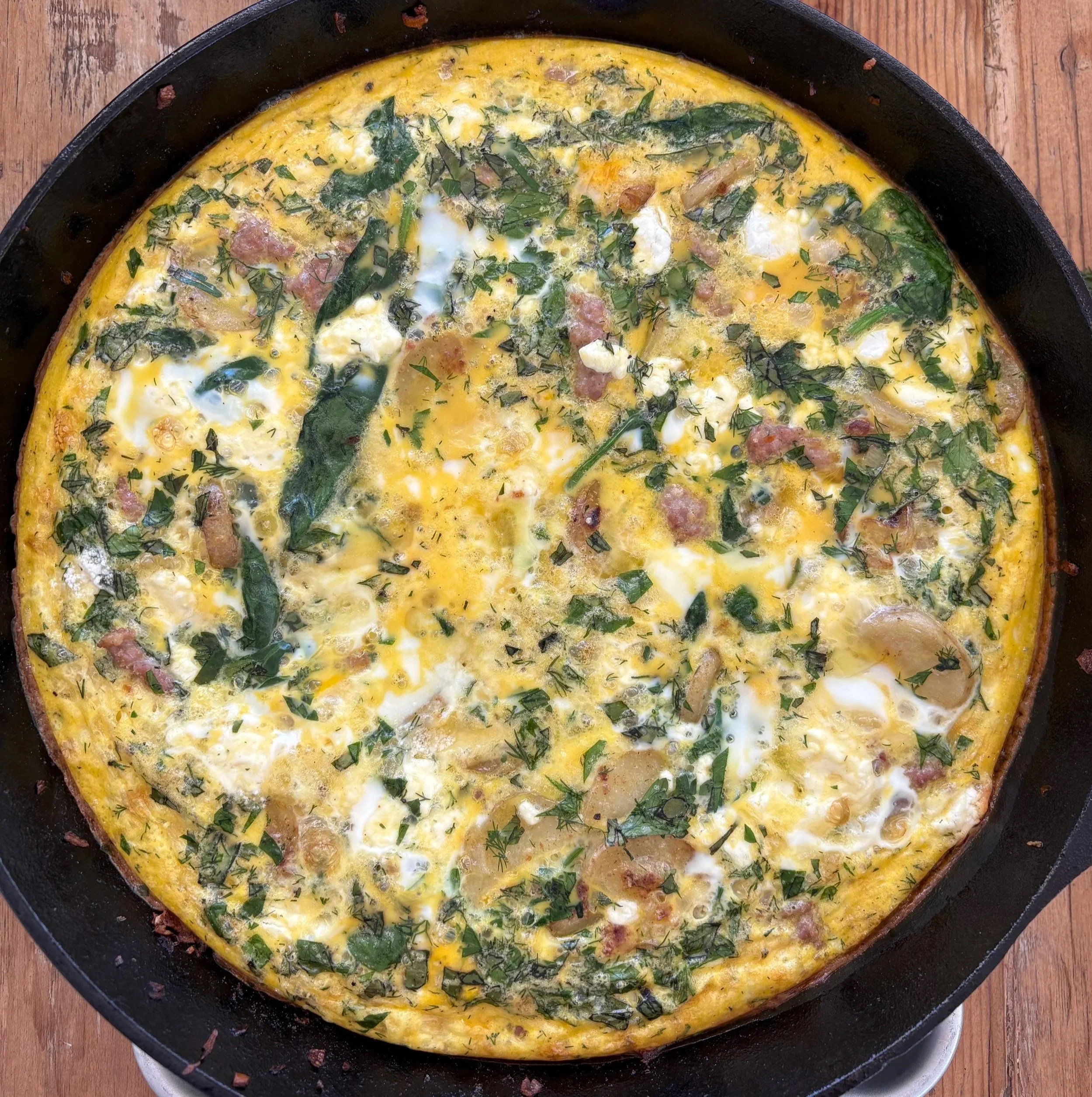 Frittata with eggs, spinach, herbs, and bacon in a skillet