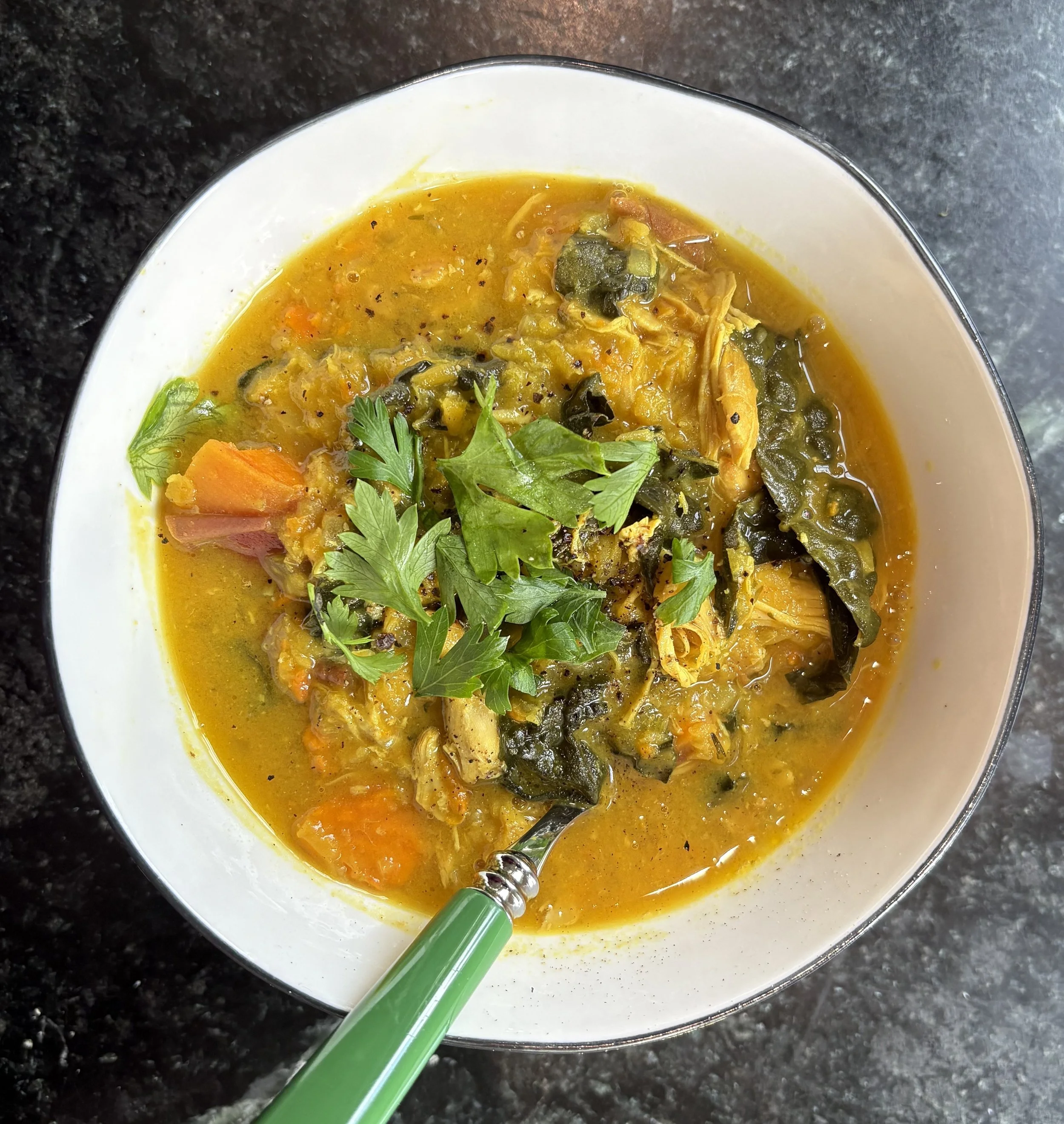 A bowl of vegetable soup with carrots, greens, and herbs garnished on top.