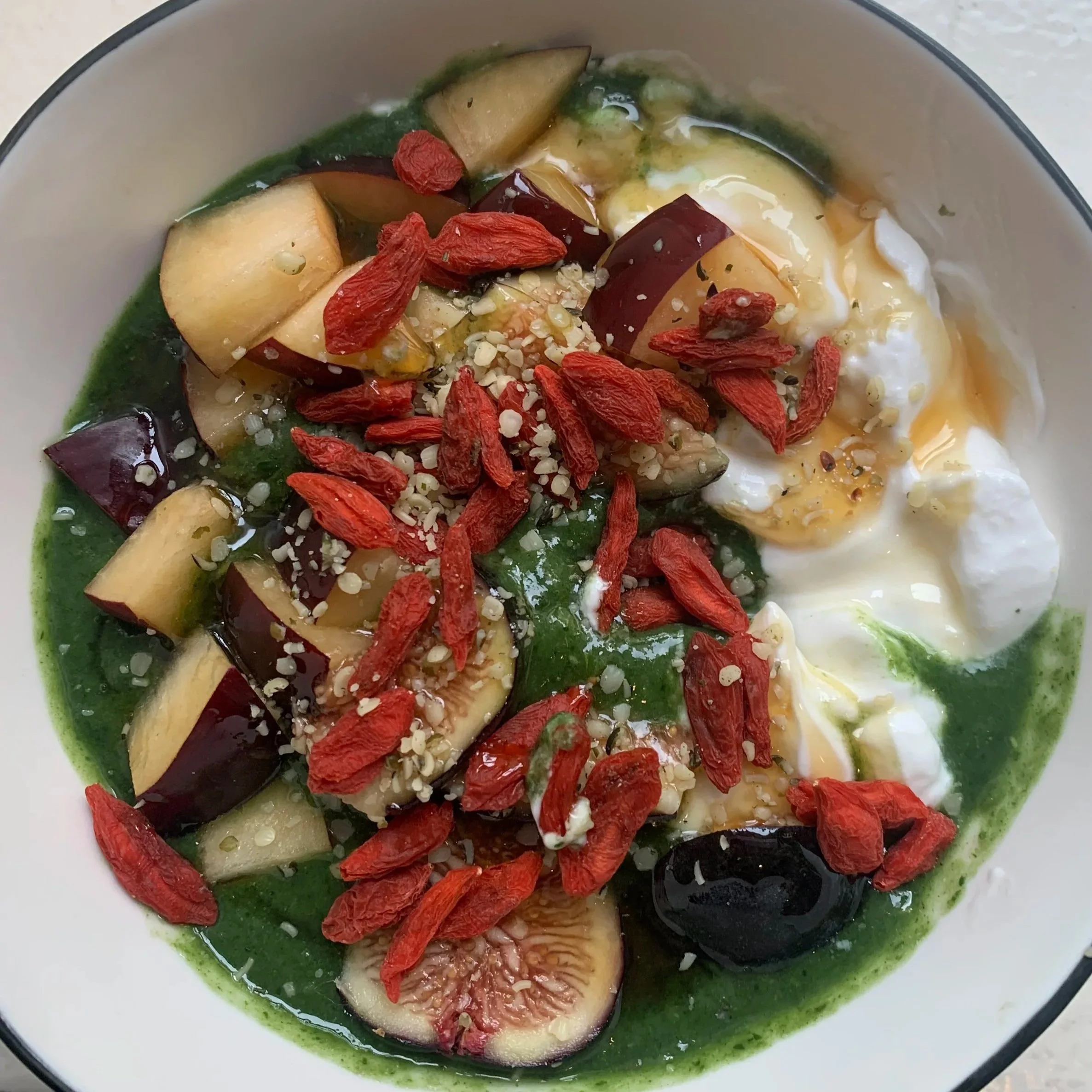 A bowl of acai smoothie topped with sliced figs, goji berries, hemp seeds, and drizzled with honey.