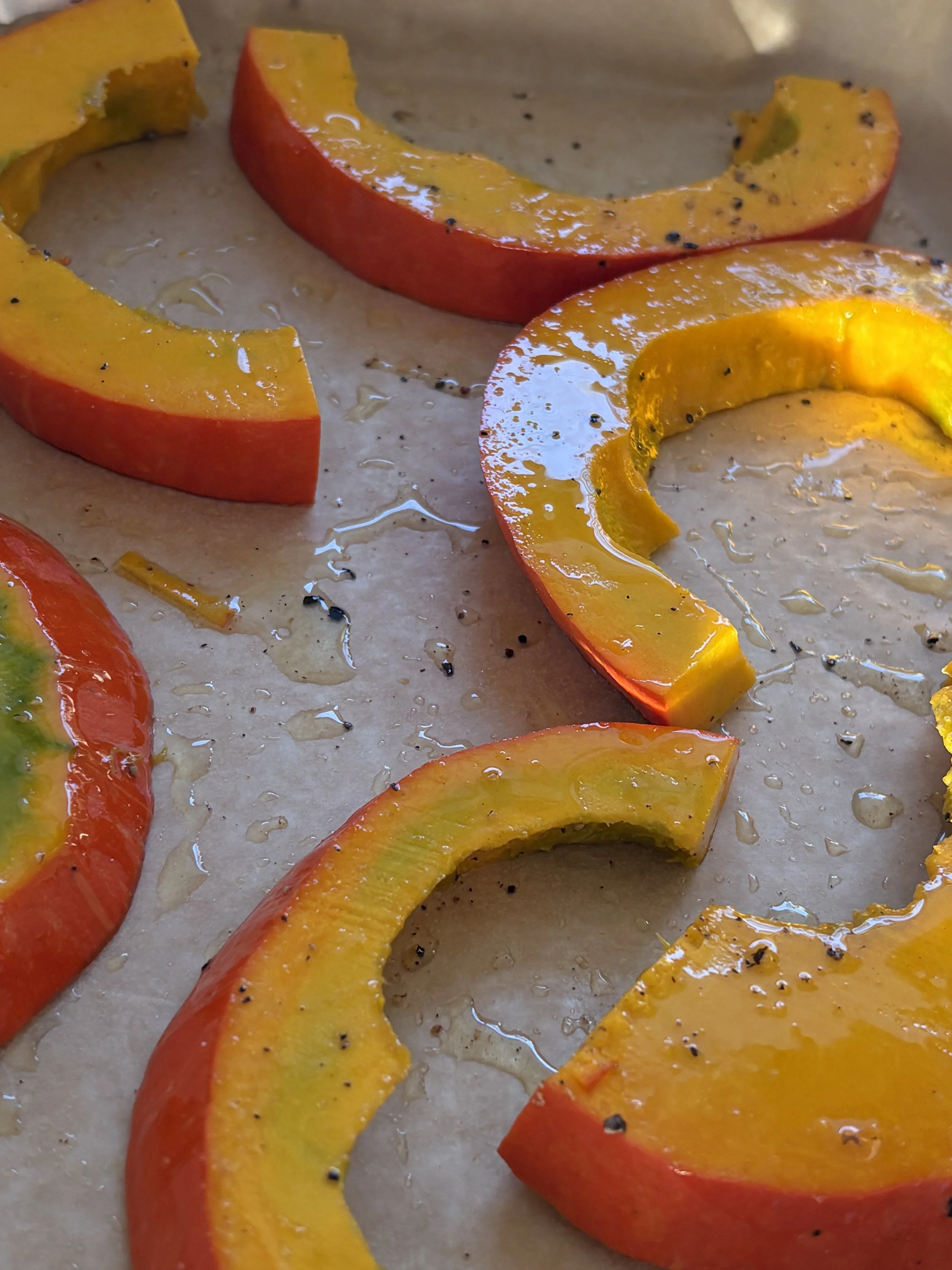 Slices of yellow and red bell peppers seasoned with black pepper and drizzled with oil on a baking sheet.