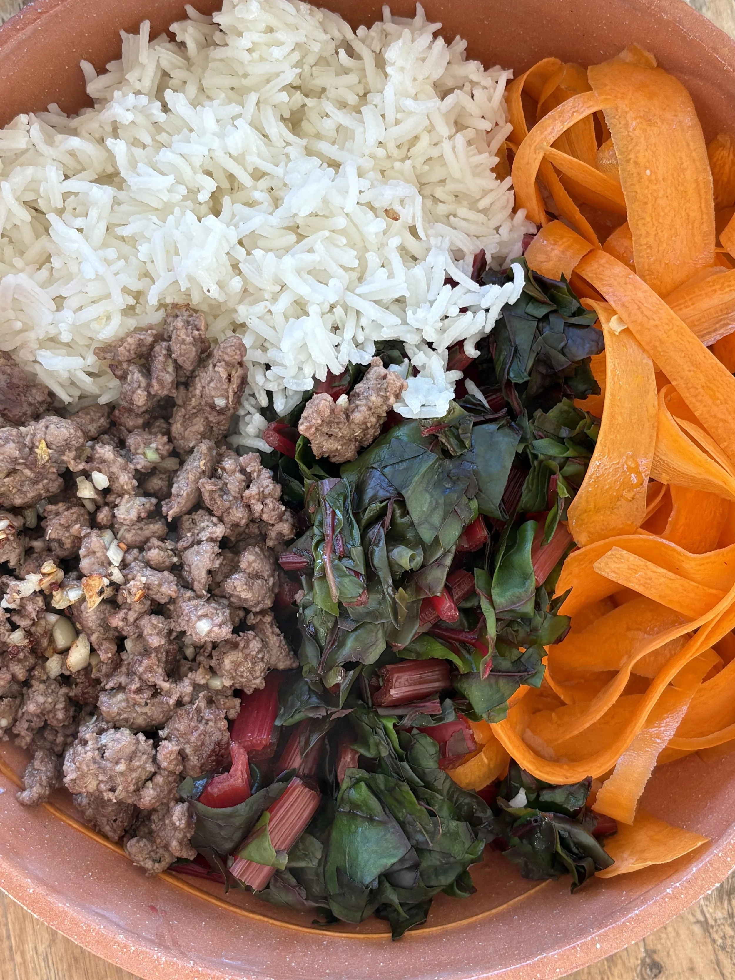 A bowl of rice with ground beef, kale, shredded carrots, and shredded red bell peppers.