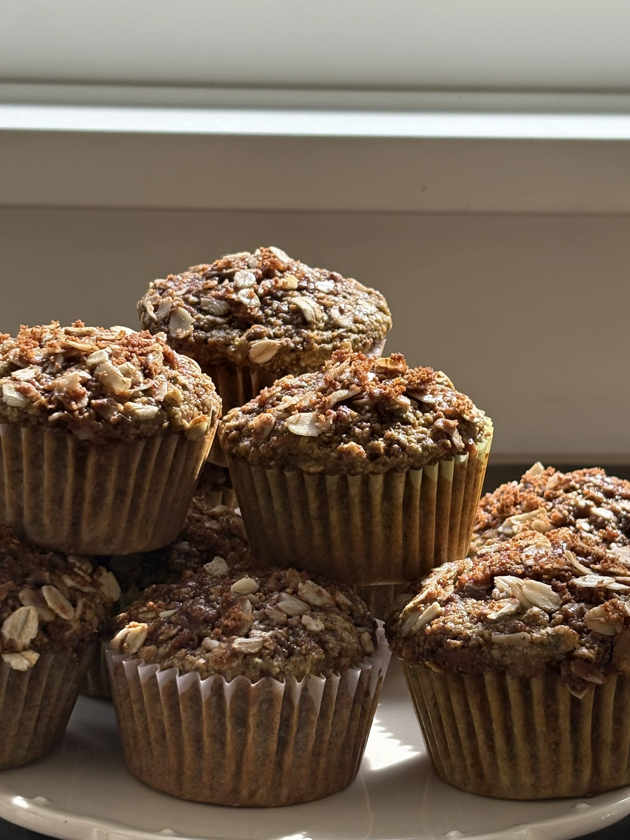 A plate of chocolate muffins with oatmeal topping, arranged near a window with sunlight.