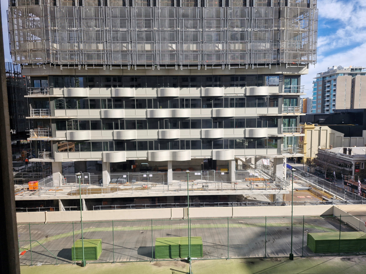 Construction site with a modern building under construction, featuring glass and white curvilinear architectural GRC elements manufactured and supplied by Satu Bumi.