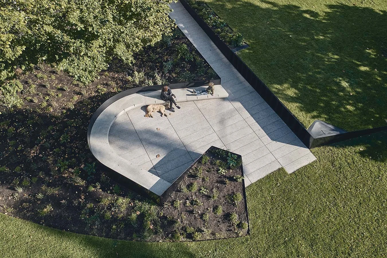 High-angle view of a custom U-shaped GRC bench with a natural aggregate finish integrated with rear planters, forming an inviting communal seating arrangement within a landscaped public space.