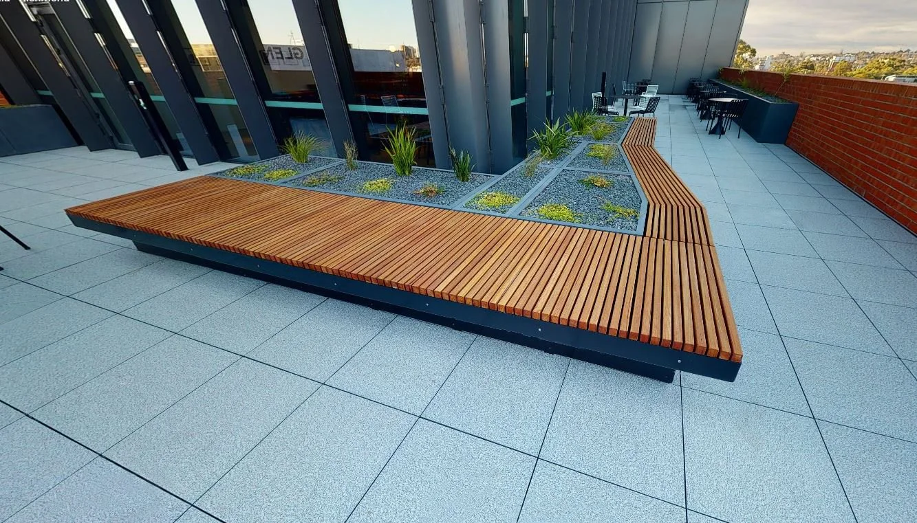 Rooftop terrace of a commercial building featuring custom charcoal pigmented GRC planter benches and rectangular GRC planters arranged to create a landscaped outdoor space.