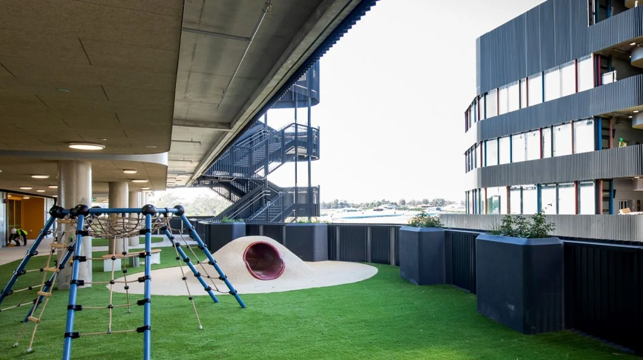 Elevated view of a college building showcasing rows of black GRC planter boxes installed beside vertical metal railings, creating a landscaped architectural facade.