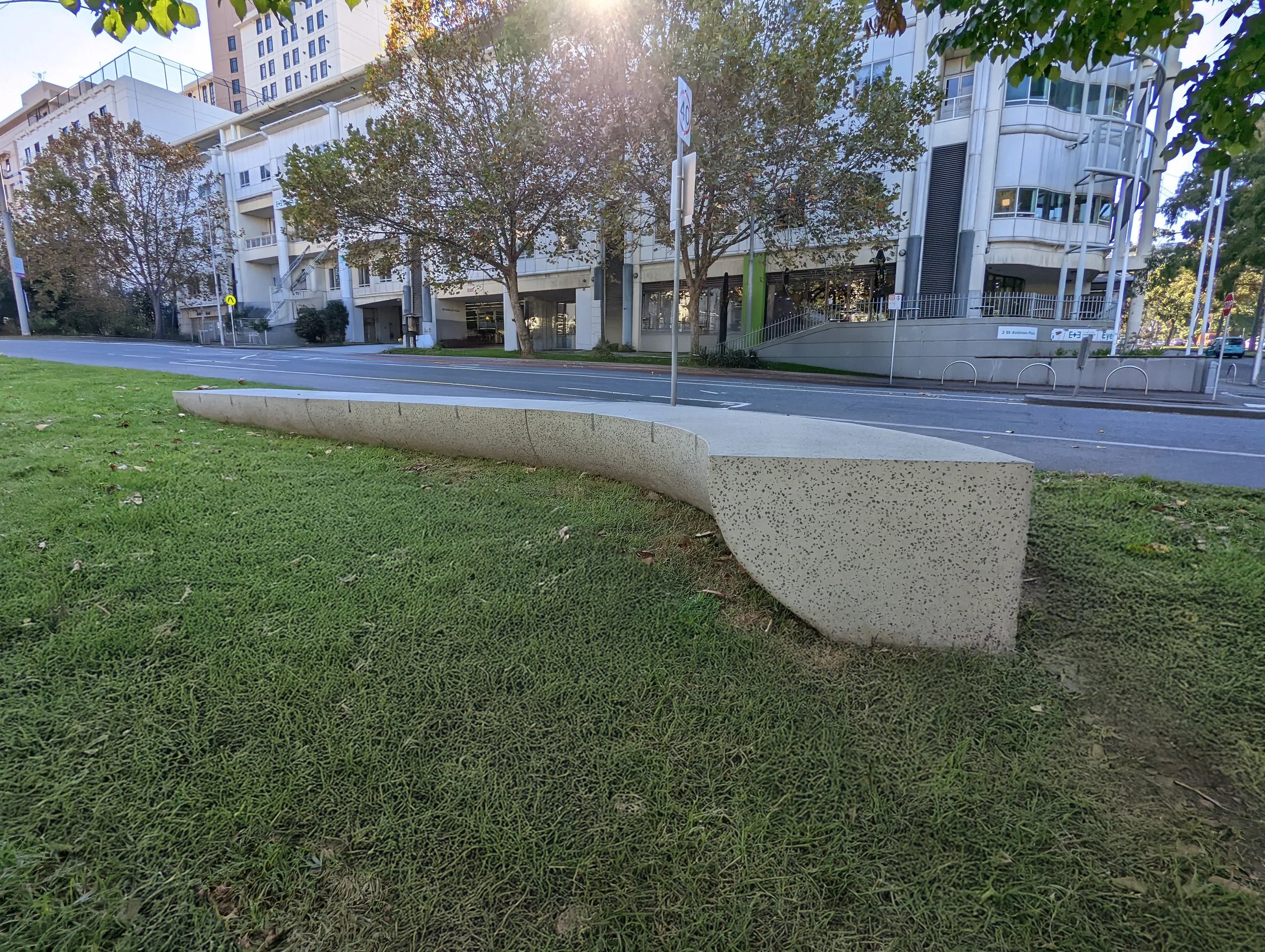 Long curved GRC bench with a natural smooth aggregate finish installed within a public landscape, providing durable contemporary seating for streetscape environments.