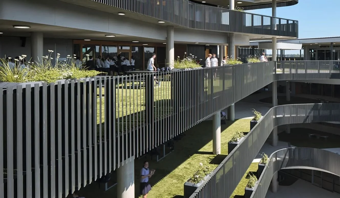 Black GRC planter boxes installed beside vertical metal balustrades along the upper levels of a college building, adding greenery to the multi-storey facade.