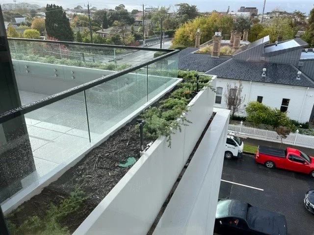View from a balcony showing a rooftop garden with plants and GRC planters from Satu Bumi connected to glass balustrades.