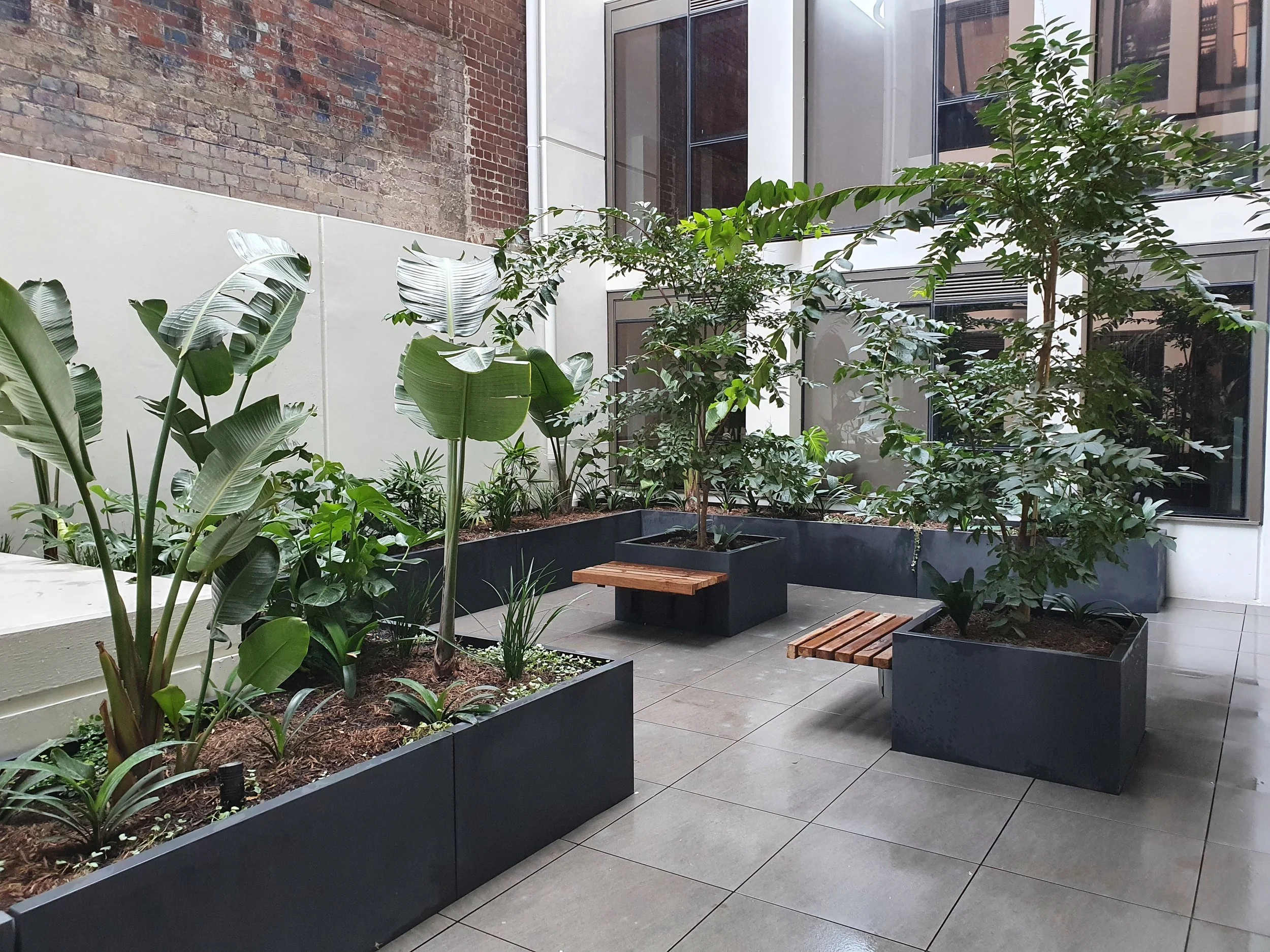 Custom charcoal pigmented GRC rectangular planters with cantilevered timber bench seating, creating an integrated landscape feature with a continuous planter design.