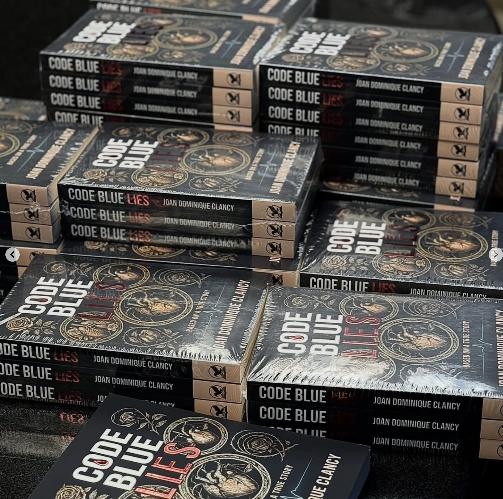 Multiple stacked copies of the book titled 'Code Blue Lies' by Joan Dominique Clancy, displaying the cover which features artwork with circular designs and a dark background.