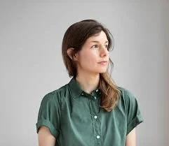 Person wearing a green button-up shirt looking to the side against a plain background.