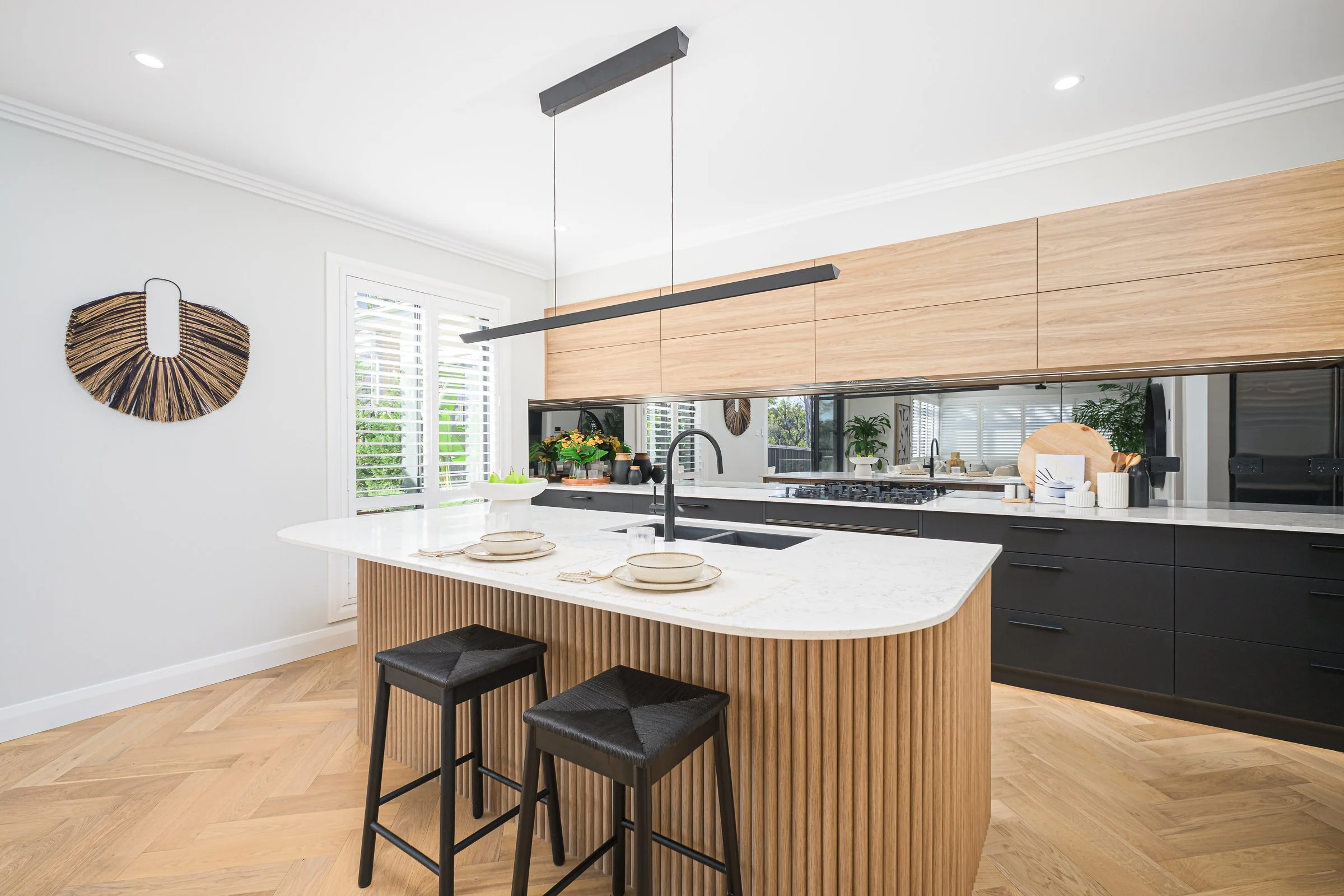 Modern kitchen with a white marble island, black and wood cabinets, and decor with green plants and woven wall art.