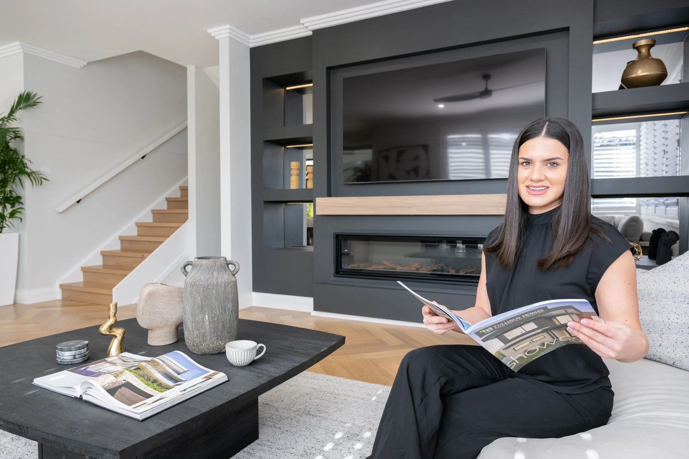 young woman dressed in business attire sitting on a lounge reading a magazine