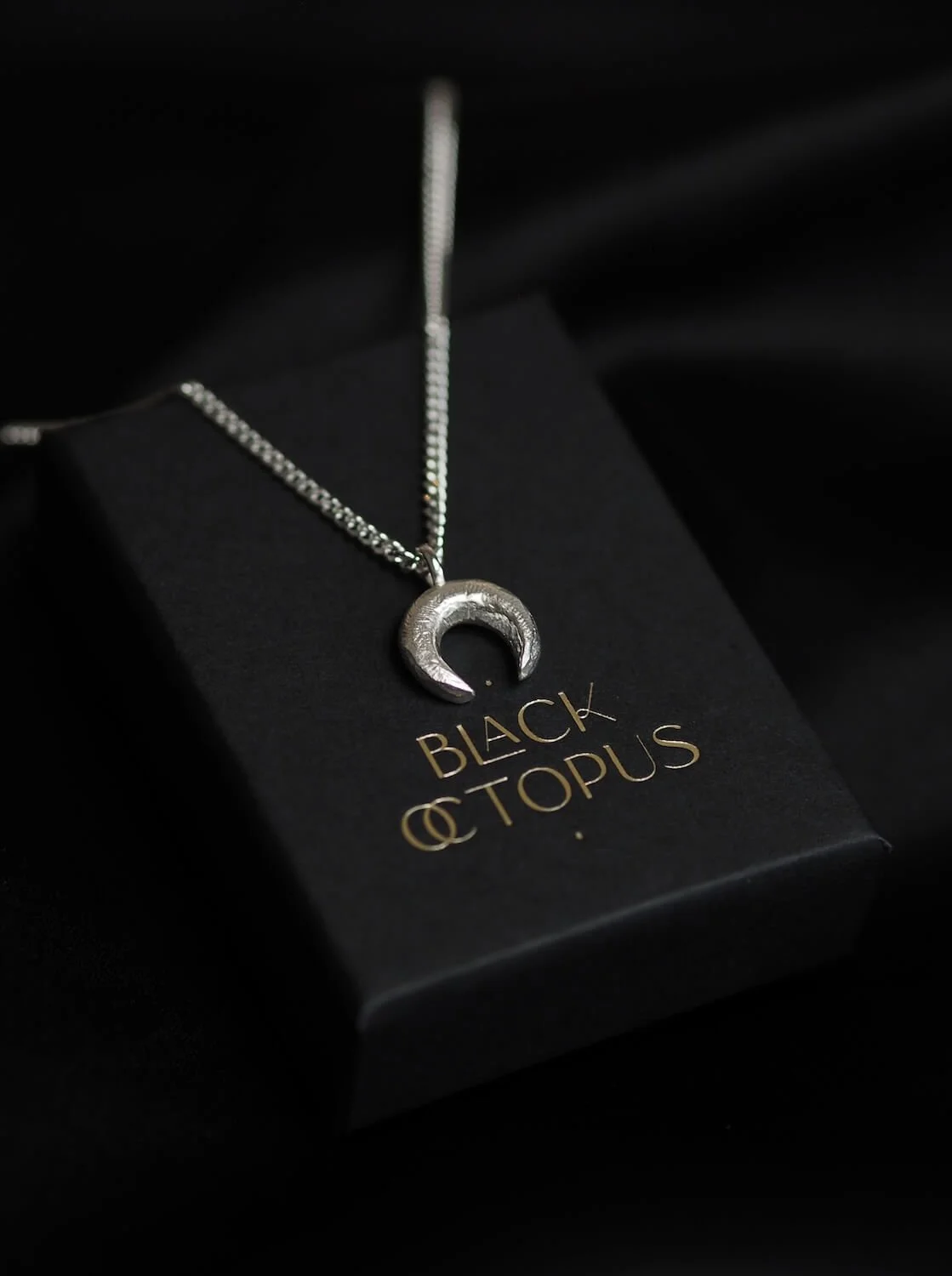 Silver crescent moon necklace with textured pendant displayed in a Black Octopus Jewellery box