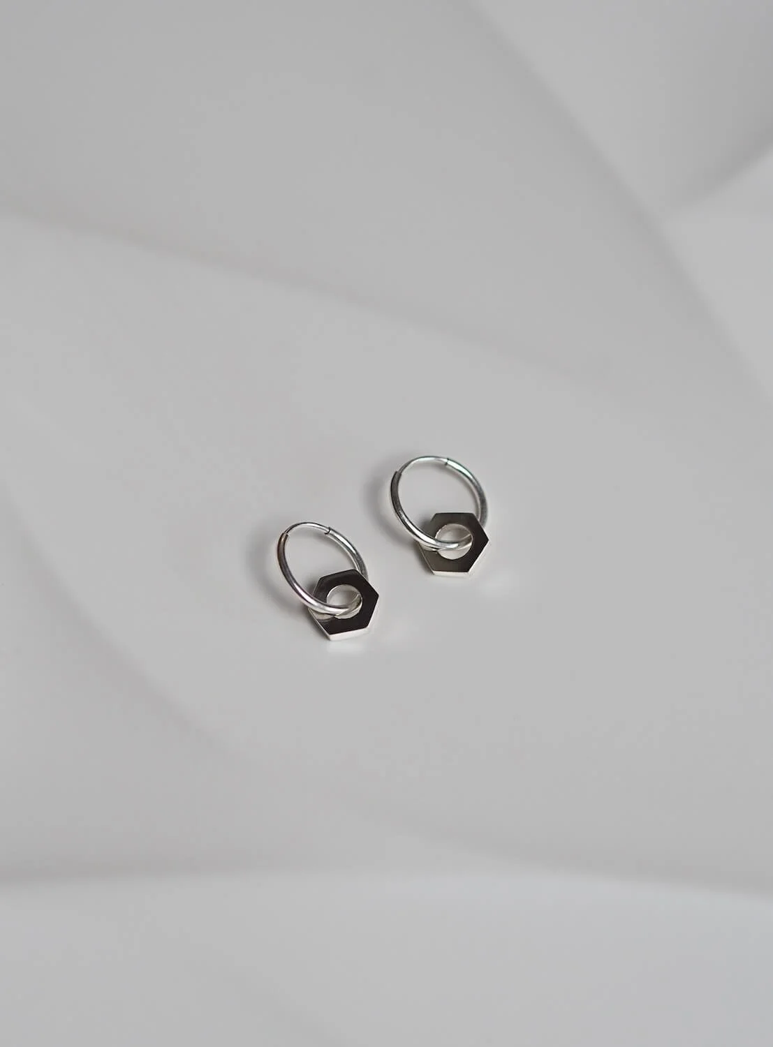 Silver endless hoop earrings with a hex nut pendant